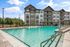 Modern apartment complex showcasing a sparkling swimming pool with sun loungers, surrounded by beautiful greenery and stylish architecture.