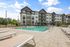 Luxurious apartment complex with modern architecture, featuring a sparkling outdoor pool and spacious sun deck, surrounded by lush greenery.