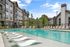 Elegant apartment complex with luxurious outdoor pool, sun loungers, and modern architecture, surrounded by lush greenery.