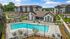 Aerial view of an upscale apartment complex featuring a large, inviting swimming pool, surrounded by neatly arranged lounge chairs and landscaped greenery, with modern buildings and parking in the background.
