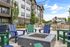 Modern apartment building with stylish outdoor seating area featuring vibrant blue and green chairs around a sleek fire pit, set against a backdrop of lush trees and a clear sky.