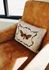 Cozy living space with a rustic tan armchair adorned with an artistic butterfly-themed pillow, infused with natural light.