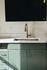 Modern kitchen area with elegant green cabinetry, sleek marble countertop, and stylish brass faucet.