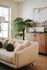 Chic living room featuring a plush cream sofa with decorative green cushions, a large leafy plant, and stylish wooden cabinet showcasing modern decor.