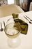 Elegant dining setup with a chic glass, stylish dark cutlery, and a neatly folded green napkin, creating a sophisticated ambiance.