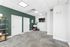Bright and modern office space featuring a green accent wall, sleek shelving unit, and wall-mounted TV, perfect for professional settings.
