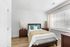 Bright and inviting bedroom featuring a cozy bed with stylish pillows, wooden nightstands, and large window with blinds.