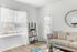 Elegant living room featuring chic decor, a comfortable sofa with decorative cushions, natural light streaming through sheer curtains, and stylish shelving.