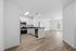 Bright open-concept apartment showcasing a modern kitchen with stainless steel appliances, adjacent to a spacious living area with beautiful wood flooring and ceiling fan, leading to a balcony.