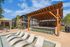 Luxurious outdoor lounge area featuring a modern pool with sleek sun loungers, shaded pergola with stylish seating, and lush greenery in a contemporary apartment setting.