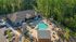 Aerial view of luxurious apartment complex featuring a resort-style swimming pool, elegant outdoor seating, and lush green trees.