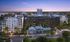Modern urban apartment complex with lush landscaping, ample parking, and a serene waterfront view at sunset.
