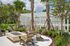 Chic outdoor patio with Adirondack chairs encircling a modern fire pit, nestled among palm trees and vibrant greenery.