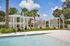 Luxurious poolside area with stylish cabanas, surrounded by lush palm trees under a clear blue sky.
