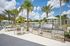 Luxurious outdoor grilling area with modern stainless steel BBQs, surrounded by palm trees and elegant seating under blue skies.