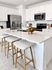 Bright and modern kitchen with sleek white cabinets, stainless steel appliances, and a chic breakfast bar with three stools.