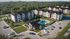 Attractive modern apartment complex surrounded by lush greenery, featuring a sparkling pool area with lounging chairs and well-maintained landscaping.
