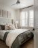 Inviting bedroom with soft, neutral tones, elegant artwork, and cozy bedding illuminated by natural light through large windows.