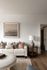 Contemporary living room with a chic white sofa adorned with patterned pillows, warm wooden table, modern art on the wall, and soft lighting creating a cozy ambiance.