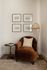 Cozy reading nook with a plush brown armchair, elegant side table, and stylish floor lamp, accented by framed art on the wall.