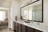 Luxurious modern bathroom featuring a double vanity with elegant faucets, a large mirror, and a walk-in shower, adjacent to a cozy bedroom with soft lighting.
