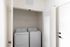 Bright apartment laundry area featuring a modern washer and dryer with ample shelving space.