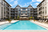Luxurious apartment complex with a sparkling pool, surrounded by elegant multi-story buildings and relaxing lounge chairs.