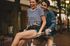 Joyful couple enjoying a fun bicycle ride through a tree-lined street, exuding happiness and youthful energy.