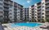 Luxurious apartment complex with modern balconies and a sparkling pool under a clear blue sky.