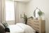 Inviting bedroom with elegant decor, featuring a cozy bed, chic dresser with a round mirror, and lush greenery.