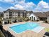 Luxurious apartment complex featuring a sparkling resort-style pool, stylish lounge areas, and modern architecture under a clear blue sky.
