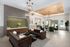 Modern living room with stylish chandeliers, sleek dark sofas, green accent chairs, and floor-to-ceiling windows offering abundant natural light.