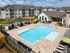 Luxurious apartment complex with a sparkling pool, surrounded by modern buildings and shaded lounge areas, perfect for relaxation and leisure.