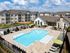 Luxurious apartment complex with a sparkling outdoor pool, surrounded by elegant loungers and shaded cabanas, set against a backdrop of stylish modern buildings.