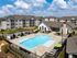 Elegant apartment complex featuring modern architecture, luxurious outdoor pool, and spacious lounge areas under clear blue skies.