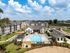 Luxurious apartment complex with a stunning outdoor pool, surrounded by modern buildings and lush landscaping.