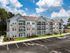 Elegant three-story apartment building with modern architecture, featuring balconies and lush landscaping, under a bright blue sky.