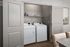 Modern laundry nook with washer and dryer, enhanced by neat shelving and elegant gray cabinetry.
