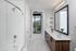 Modern bathroom featuring sleek wood cabinetry, a spacious countertop with decorative flowers, subway tile shower, and a large mirror reflecting a bright and airy atmosphere with a view of the balcony.