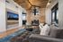 Luxurious living room with plush gray sofa, chic wooden accents, modern fireplace, and large windows offering stunning cityscape views.