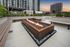 Modern urban outdoor space featuring a sleek fire pit surrounded by stylish seating and lush greenery, set against a stunning cityscape twilight backdrop.