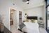 Modern bedroom with stylish decor including gold accents, large windows offering natural light, and an adjoining walk-in closet and bathroom.