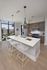 Modern kitchen with sleek white island, stylish pendant lighting, and floor-to-ceiling windows offering a city view.