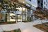 Elegant entrance of a modern apartment building with large glass windows and lush landscaping.