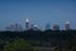 Captivating city skyline at dusk with iconic illuminated skyscrapers, nestled above lush green treetops.