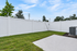 Inviting backyard view featuring lush green grass, a neatly paved patio, and a charming white privacy fence under a bright blue sky.