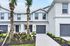 Charming modern townhouse with two stories and manicured landscaping, featuring twin palm trees and a sleek exterior design.