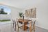 Bright dining area with a chic wooden table, modern woven chairs, and elegant wall art, overlooking a lush green garden.