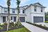 Modern townhouse exterior featuring elegant white siding, two-car garage, and lush landscaping with palm trees and vibrant flowers.