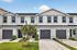 Charming townhouse facade with modern architecture, featuring three garages and manicured landscaping under a clear blue sky.